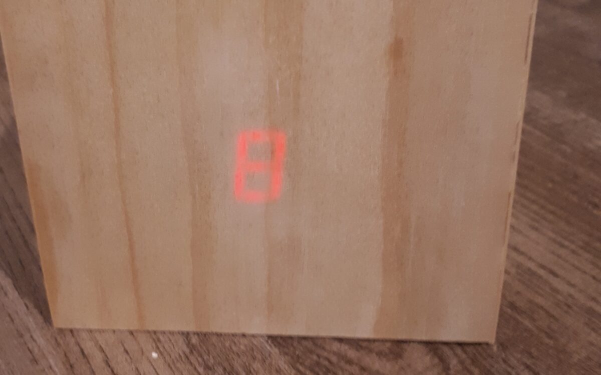 A wooden box sits on a darker wooden table. The box has a red, glowing number 8 on it.